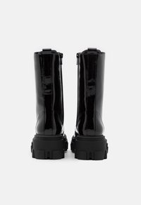 Paire de bottes de combat en cuir verni noir brillant avec des semelles épaisses et épaisses vues de dos sur un fond blanc.