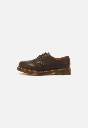 Donkerbruine leren veterschoen met gele stiksels en dikke rubberen zool, getoond vanaf de buitenkant op een witte achtergrond.