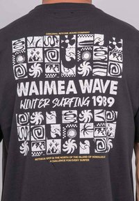 T-shirt noir avec des motifs graphiques et du texte blancs. Le design comprend des carrés avec divers motifs géométriques et en spirale.