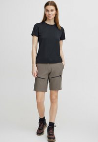 Lühikeste varukatega must T-särk, millele on sobitatud beežid lühikesed püksid, millel on kaks lukuga esikot. Komplekti kuuluvad ka pruuni ja musta värvi matkajalatsid, millel on nööbid.