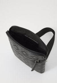Black crossbody bag with a geometric embossed pattern, zip closure, and a smooth interior. Features an adjustable strap for versatility.