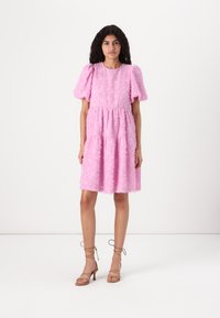 Vestido curto rosa feito de tecido texturizado, com mangas bufantes, cintura ajustada e saia rodada, terminando logo acima do joelho.