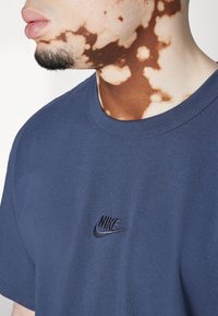 Marinblå bomulls t-shirt med rund hals, med en liten svart broderad Nike-logotyp på bröstet. Slät textur, vanlig passform.
