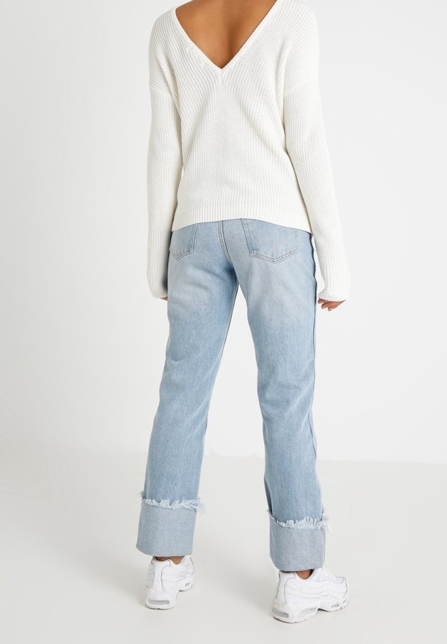 V-paittu valkoinen neule, joka on yhdistetty vaaleansinisiin farkkuihin, joissa on rispaantuneet helmat, ja valkoisiin tennareihin. Pehmeä rakenne ja rento istuvuus.