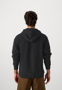 Svart huvtröja med långa ärmar och ribbade muddar, med en enkel design och avslappnad passform, bärs med bruna byxor.