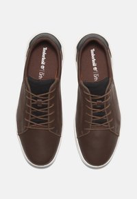 Bruna lädersneakers med svarta nätaccenter, vit gummisula och sex bruna öglor på snörningen fram. Ortholite-inlägg för komfort.