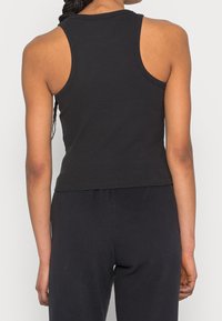 Svart ribbad linne med en figurnära design, breda axelband och en kortad nederdel. Tillverkad av mjukt, stretchigt tyg för komfort.