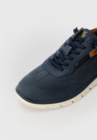 Ναυτικό δερμάτινο αθλητικό παπούτσι με τρυπητό σχέδιο, υφασμάτινη επιφάνεια, αντίθετη λευκή σόλα και καφέ λεπτομέρεια στη γλώσσα. Διαθέτει κλείσιμο με κορδόνια.