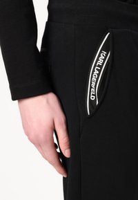 Black jogger pants with side pockets, featuring a white logo accent and textured fabric near the cuffs. Focus on comfort and functionality.