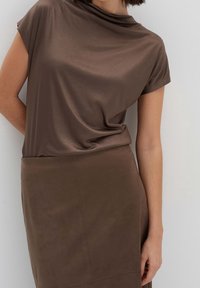 Haut marron à manches courtes avec un col drapé, associé à une jupe en daim marron assortie, présentant une texture lisse et un design simple.
