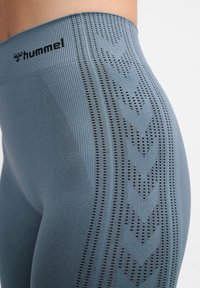 Blaue Sportleggings aus strukturiertem Stoff, mit vertikalen Streifen und einem Zickzackmuster. Das Markenlogo ist auf dem Bund angebracht.