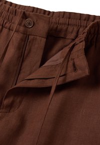 Pantaloni di lino marrone con vita elastica, chiusura frontale con zip e bottone, e dettagli con coulisse. Tessuto liscio e vestibilità comoda.