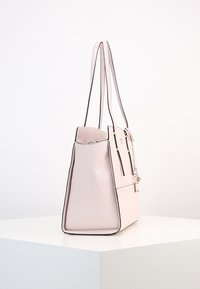 Light pink structured handbag with long handles, black trim, subtle embossed pattern, and gold-tone hardware, displayed on white pedestal.