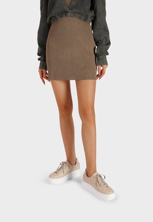 Gonna mini a coste marrone abbinata a un maglione corto verde scuro e sneakers beige con zeppa e suole e lacci bianchi.