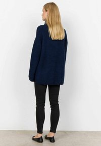 Navyblå oversized tröja i stickad väv med texturerad yta, kombinerad med svarta slim-fit byxor och svarta platta skor.