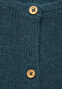 Stickad teal-färgad cardigan med ribbmönster och två träknappar med mörka korsmönster som framhäver funktionella detaljer.