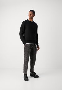Suéter negro de punto, pantalones grises a rayas y zapatos negros con cordones. Diseño simplista, textura suave, corte relajado y sutiles contrastes de color.