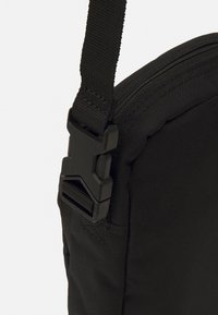 Primo piano dell'angolo di una borsa di tessuto nera con una tracolla regolabile e una fibbia in plastica a rilascio laterale.