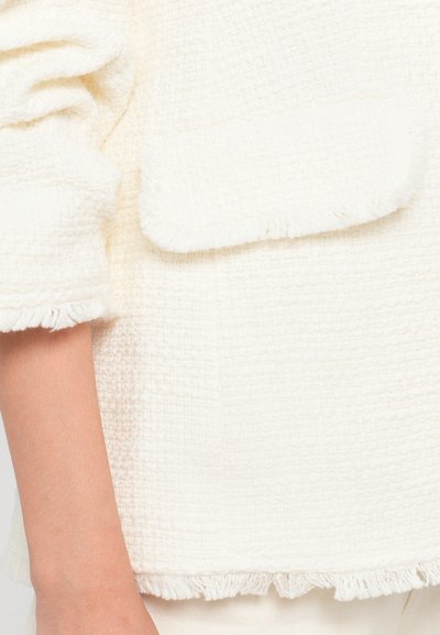Witte textuurstof met een zachte, geweven uitstraling. Heeft een franjezoom en een opgestikte zak aan de voorkant. Casual, relaxed fit ontwerp.