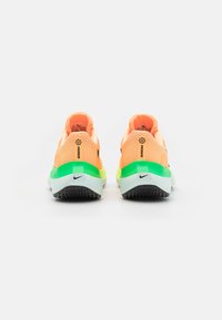 Une paire de chaussures de course orange avec des semelles intermédiaires vertes et jaunes, des semelles extérieures noires et des logos Nike noirs, présentée de dos sur un fond blanc.