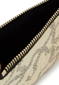 Monedero con cremallera en blanco y negro, con un diseño estampado, herrajes dorados y un interior forrado en negro. Presenta una superficie suave y un diseño intrincado.