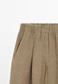 Kalhoty z lněného materiálu v khaki barvě s texturovaným povrchem, s nařaseným pasem a bočními záhyby pro větší detaily a pohodlí.