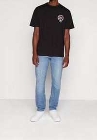 Černé bavlněné tričko s malým barevným logem na hrudi, spárované s světle modrými džíny a bílými teniskami.