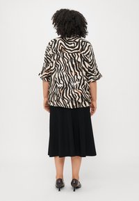 Blouse à manches courtes imprimée zèbre, présentant des tons beige, noir et marron, associée à une jupe noire et des chaussures à talons.