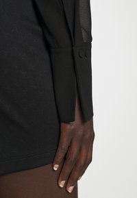 Czarna koszula z przezroczystymi rękawami, dopasowanym krojem, teksturowanym materiałem z subtelnym wzorem oraz guzikami na mankietach.