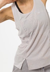 Lichtgrijs sporttanktop met meshpanelen, textuurstof en subtiele print. Heeft een losse pasvorm en een zijsplit voor ademend vermogen.