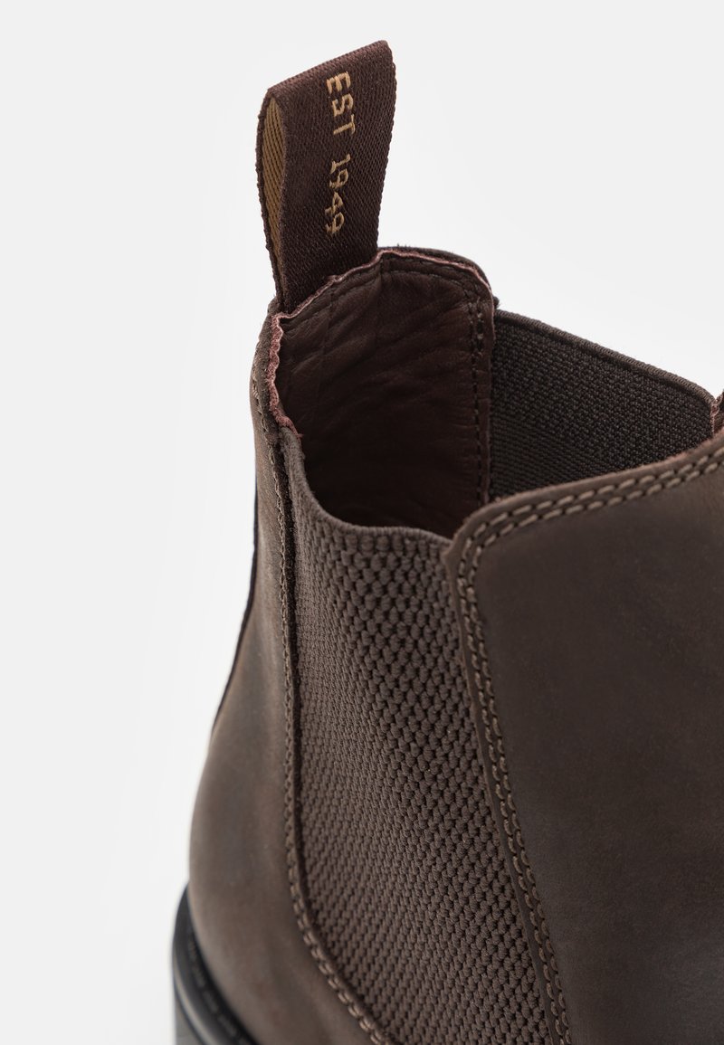 Nahaufnahme eines braunen Leder-Ankle Boots mit elastischem Seitenpaneel und Stoff-Ziehlasche, auf der der Text "EST 1949" zu sehen ist.