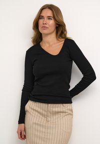 Sort langærmet top med V-hals, ribbet tekstur, tætsiddende design. Matchet med en beige stribet nederdel, der har lodrette linjer og skræddersyet pasform.