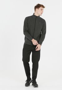 Mørkegrå lynlåsjakke med høj krave, sammen med sorte tapered bukser. Outfittet har en glat overflade og minimalistisk design.