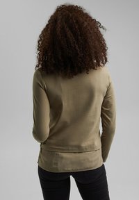 Langärmliges Oberteil in Olivgrün, aus glattem Stoff gefertigt. Verfügt über einen runden Ausschnitt und eine taillierte Silhouette mit einem abgerundeten Saum hinten.