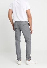 Grau gemusterte Hose mit Slim-Fit, ausgestattet mit Gesäßtaschen und einem dezenten strukturierten Design, kombiniert mit weißen Sneakers und einem schlichten weißen Hemd.