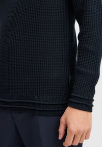 Marineblauer Strickpullover mit strukturiertem Muster, gerippten Bündchen und Saum; verfügt über ein kleines Etikett an der Seite.