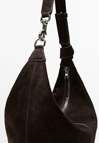 Borsa a tracolla in camoscio marrone con una forma curva, dotata di chiusura a zip e una clip metallica su una tracolla, evidenziando la sua texture morbida e il design.