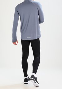 Långärmad, ljusgrå idrottströja med hög krage, ihop med svarta leggings och svarta löparskor, med reflexdetaljer.