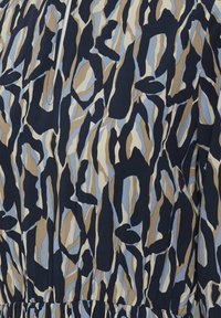 Motif camouflage abstrait avec des formes irrégulières en noir, beige, bleu clair et blanc sur un tissu froncé.