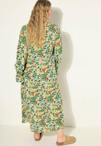 Robe maxi florale avec un fond vert et des fleurs rouges, jaunes et blanches. Manches longues avec des poignets roulés, tissu doux, coupe décontractée.