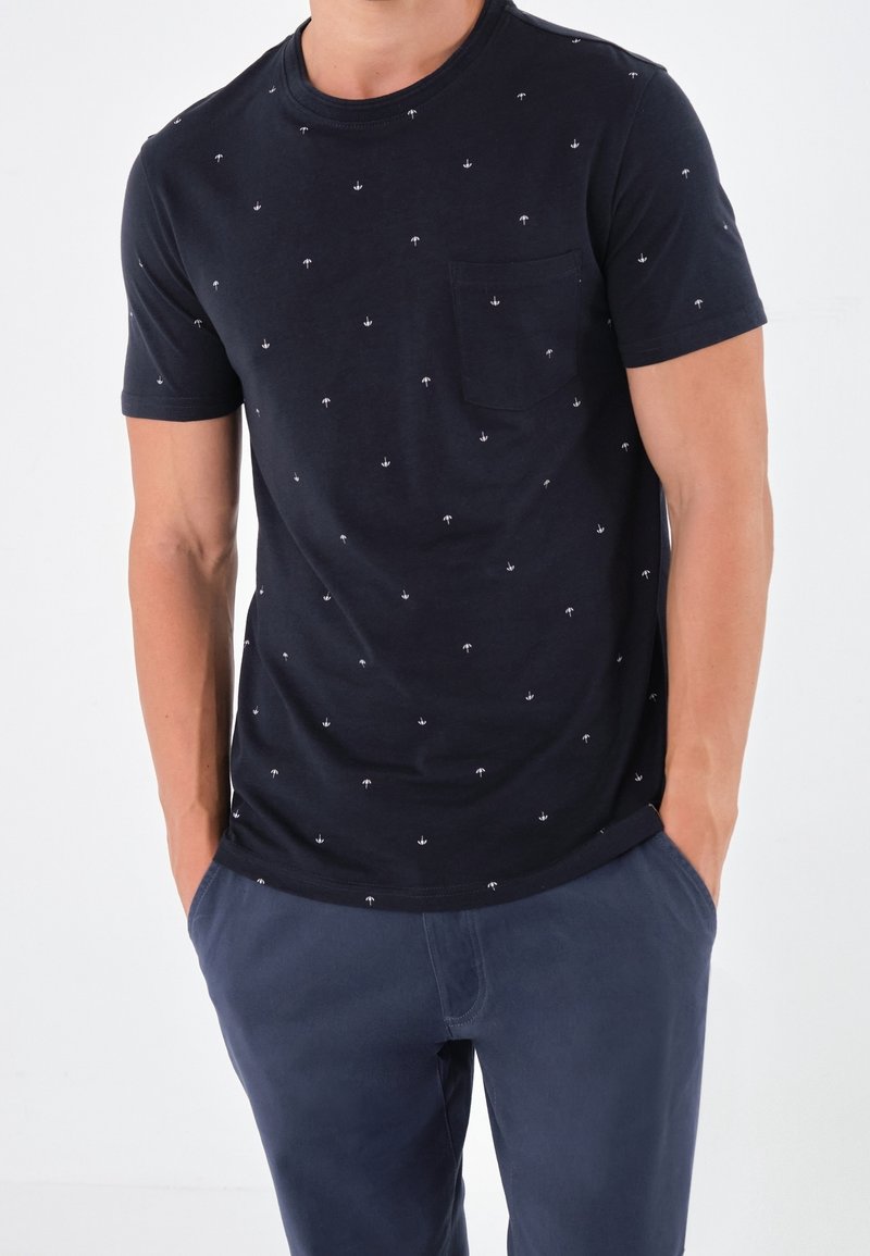 Marinblå bomullströja med små vita palmträdsmönster, rundad halsringning, korta ärmar och en bröstficka till vänster, i kombination med marinblå byxor.