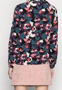 Blouse florale à manches longues en tissu sombre avec des fleurs rouges, violettes et teal ; associée à une jupe en velours côtelé rose clair.