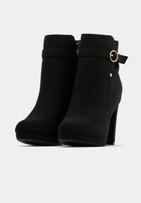 Juodi kulkšneliai pagaminti iš tekstūruoto medžiagos, su šoniniu užtrauktuku, auksiniu akcentu ir aukšta kulno dizainu.