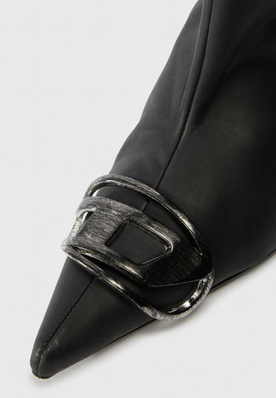 Chaussure noire à bout pointu en cuir lisse, avec un détail boucle métallique argentée. Le design présente des lignes épurées et une silhouette élégante.
