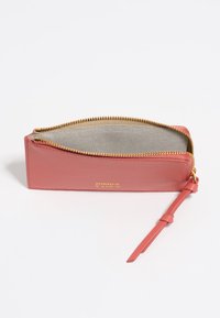 Cartera de cuero rosa con cremallera y herrajes en dorado, interior de color claro y una correa delgada. Presenta un logotipo en el exterior.