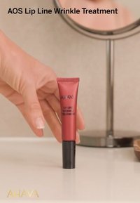 Röd tub med AHAVA Lip Line Wrinkle Treatment med en svart bas. Tuben har vit text som märker produkten. Slät textur.
