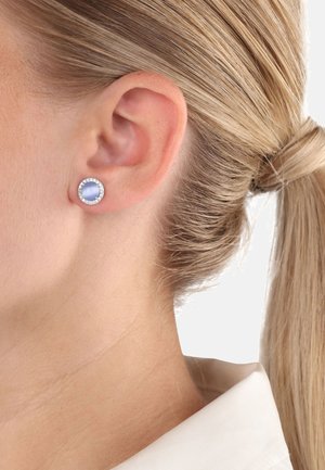Orecchini a perno rotondi con una pietra centrale di colore azzurro chiaro circondata da piccoli cristalli trasparenti, montati su una base metallica.