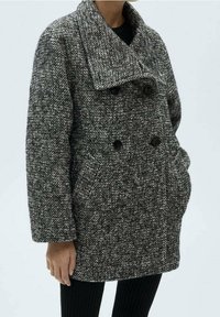 Manteau gris à motif pied-de-poule avec un grand col, boutonnage croisé et poches latérales, fabriqué en tissu tissé texturé.