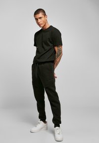 Sort bomulds t-shirt og matchende sweatpants med sidelommer, parret med hvide sneakers. Har en afslappet pasform og struktureret stof.