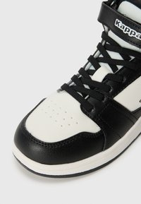 Mustvalge kõrge sneaker, millel on tekstuuriga nahkülemus, auguline varvas ja mustad paelad. Kappa logo rihmal.